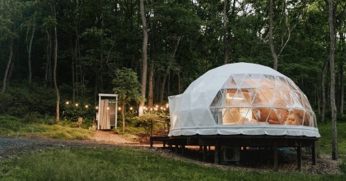 A lit white geodesic dome sits on a wooden platform in a Pennsylvania forest, surrounded by trees and string lights.