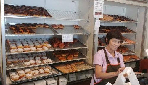 A woman prepares bags of pastries in front of a display filled with various donuts and cronut options.
