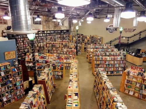 A spacious bookstore filled with tall shelves of books, organized into sections for adults and kids, under bright lights.