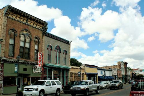 Historic buildings line a street with parked cars under a partly cloudy sky.