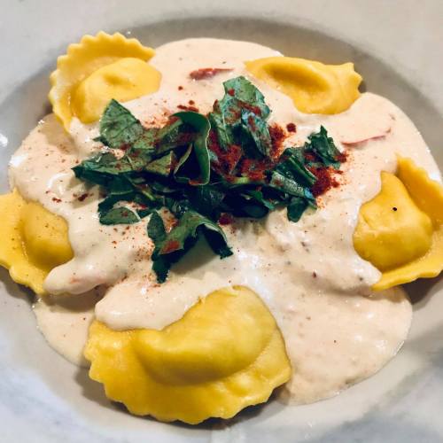 A bowl of ravioli topped with creamy sauce, herbs, and a sprinkle of paprika.