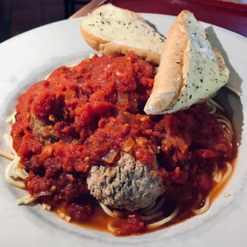 A plate of spaghetti topped with meatballs and marinara sauce, served with two slices of garlic bread.