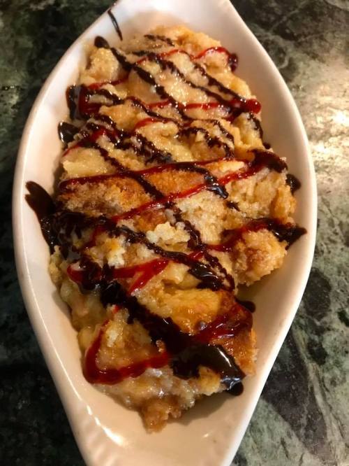 A dish of crispy fried dessert drizzled with chocolate and red sauce, served in a white boat-shaped plate.
