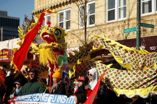 A colorful dragon dance at a parade, with participants holding banners and wearing festive attire.