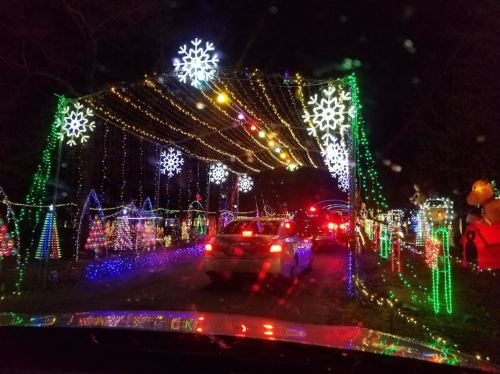 A festive display of colorful holiday lights and decorations, with cars driving through a lit archway.