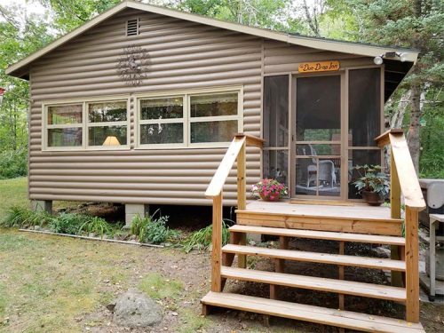 A cozy cabin with a wooden porch, surrounded by greenery, featuring a sign that reads "Dee Dee Inn."