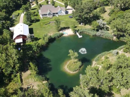 Aerial view of a serene pond surrounded by greenery, with a house and barn nearby, and a small island in the water.