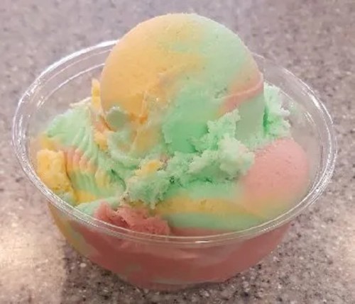 A colorful scoop of ice cream in a clear cup, featuring pastel shades of green, yellow, and pink.