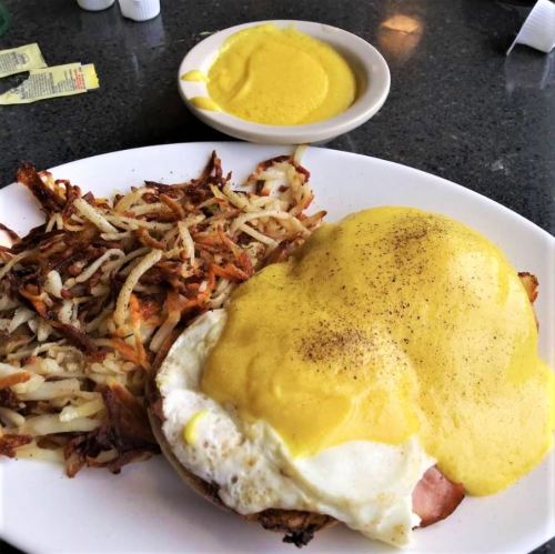 A plate of eggs Benedict with hollandaise sauce, served with crispy hash browns and a side of mustard.