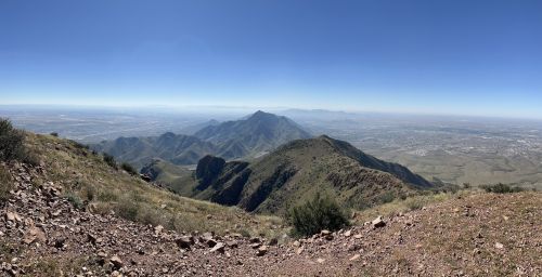 Panoramic view of mountains and valleys under a clear blue sky, showcasing a vast landscape.