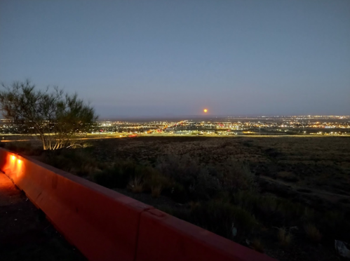 A panoramic view of a city at dusk, with lights twinkling and a faint glow on the horizon.