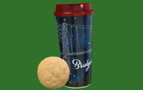 A festive coffee cup with a bridge design next to a round cookie on a green background.