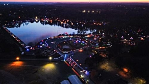 Aerial view of a lake at dusk, surrounded by colorful lights and decorations along the shore and pathways.