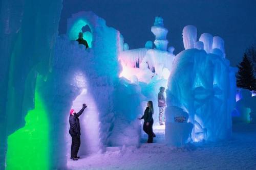 Colorful ice sculptures and structures illuminated at night, with people exploring the icy landscape.