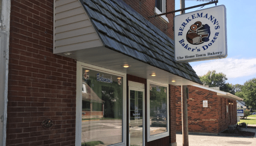 Exterior of Berklemann's Baker's Dozen bakery, featuring a sign and large windows on a brick building.