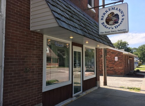 Exterior of Berkemann's Baker's Dozen bakery, featuring a sign and large windows on a brick building.