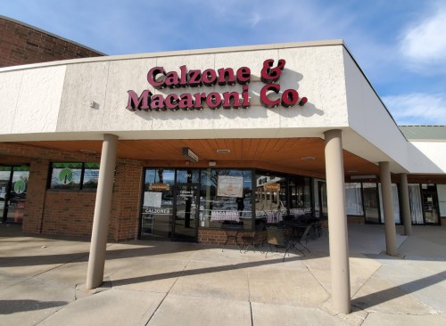 Exterior of Calzone & Macaroni Co. restaurant, featuring a sign and outdoor seating area.