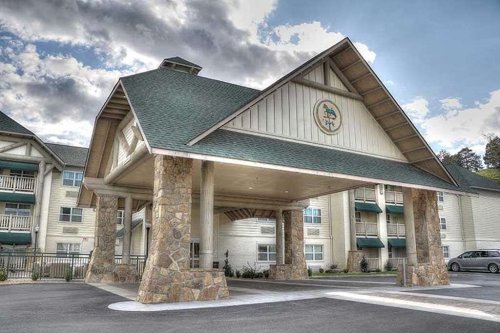 A modern lodge entrance with a stone facade and a peaked roof, surrounded by greenery and a cloudy sky.