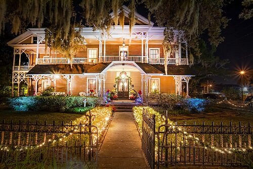 A beautifully lit historic house at night, adorned with colorful lights and surrounded by a decorative fence.