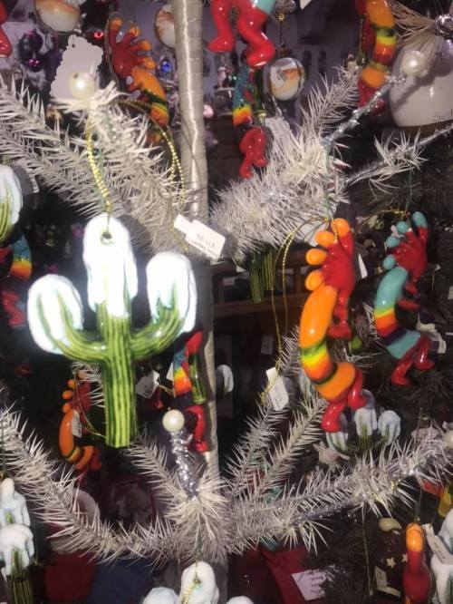 Colorful ornaments shaped like cacti and other designs hang on a silver tinsel tree.