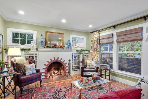 Cozy living room with a fireplace, colorful rug, plaid armchair, and decorative plants and artwork.