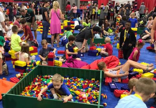 A vibrant scene of children and adults playing with colorful building blocks at a large indoor event.