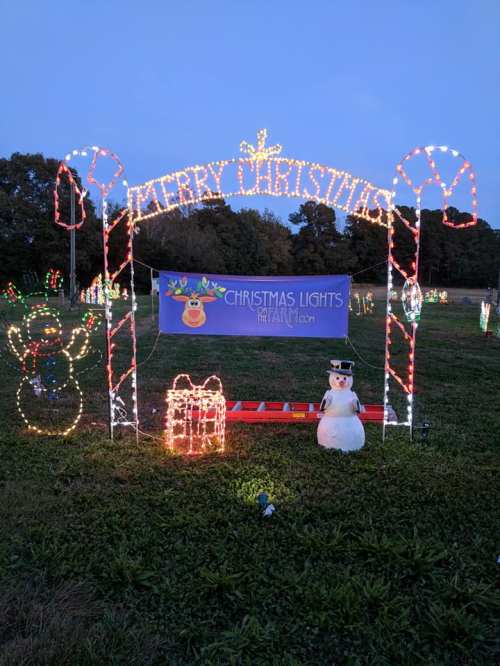 A festive display with a "Merry Christmas" arch, snowman, and colorful lights in a grassy field.