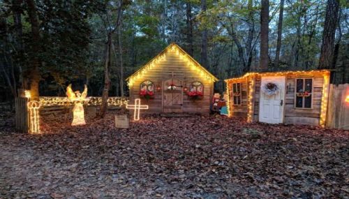 A cozy cabin decorated with festive lights and holiday decorations, surrounded by autumn leaves in a wooded area.