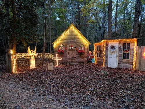 A cozy wooden cabin decorated with Christmas lights, surrounded by autumn leaves and festive decorations.