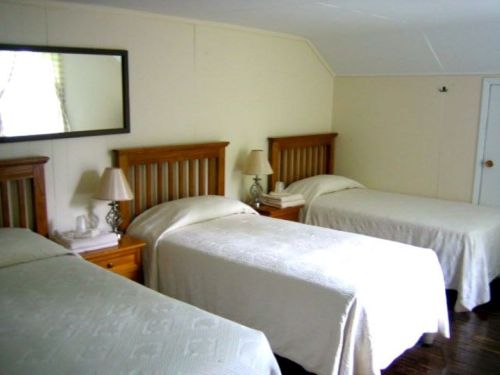 A cozy bedroom with three twin beds, wooden headboards, bedside lamps, and a mirror on the wall.