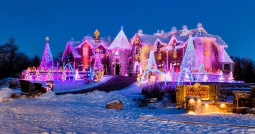 A beautifully decorated house with colorful Christmas lights and snow, featuring trees and festive displays.