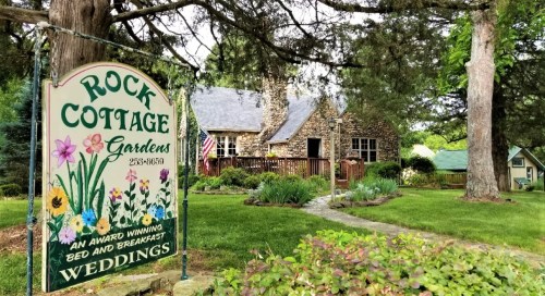 A stone cottage surrounded by gardens, featuring a sign for "Rock Cottage" and indicating it's a bed and breakfast.