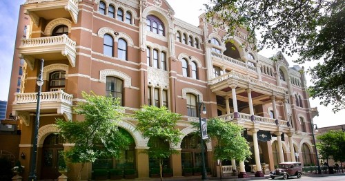 Historic building with ornate architecture, featuring balconies and large windows, surrounded by trees and a clear blue sky.