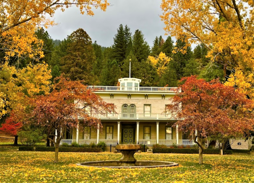 A grand, two-story house surrounded by vibrant autumn trees and a fountain in a colorful fall landscape.