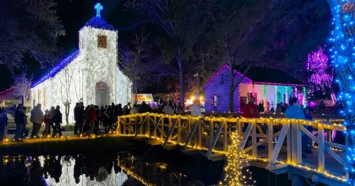 A festive scene with a brightly lit church and house, surrounded by people and illuminated trees at night.