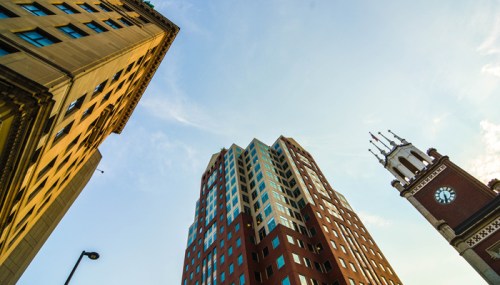 A low-angle view of tall buildings against a blue sky, featuring a clock tower in the foreground.