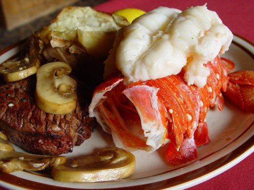 A plate featuring a baked potato, steak, lobster tail, and sautéed mushrooms.