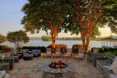 A serene lakeside patio with lounge chairs, a fire pit, and lush trees, creating a relaxing outdoor space.