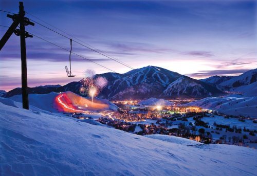 A snowy mountain landscape at dusk, featuring a ski lift and colorful fireworks over a lit-up town below.