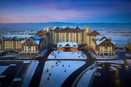Aerial view of a large hotel surrounded by snow, with mountains in the background and a clear sky at dusk.