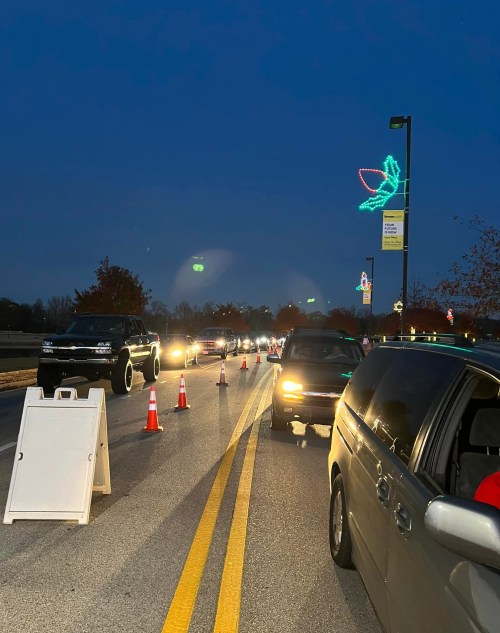 Cars lined up in a dark setting with traffic cones and holiday lights in the background.