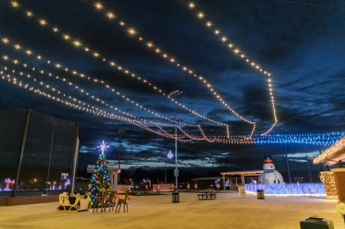 A festive scene with a decorated Christmas tree, lights strung across a dark sky, and a snowman in the background.