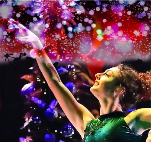 A dancer in a green costume performs gracefully against a colorful, festive background of lights and sparkles.