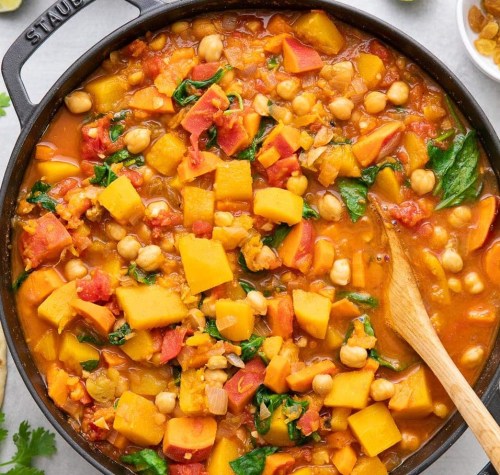 A colorful vegetable stew with chickpeas, spinach, and squash in a black pot, garnished with herbs.