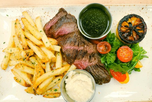 A plate featuring grilled steak, crispy fries, a side salad, roasted tomatoes, and dipping sauces.