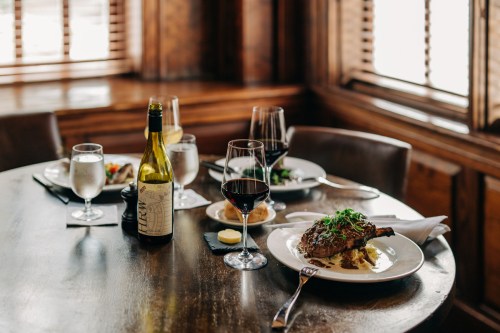 A beautifully set dining table with a plate of food, wine glasses, and a bottle of white wine in a cozy restaurant.