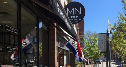 A storefront with a sign for a wine bar, featuring flags and a clear blue sky in the background.