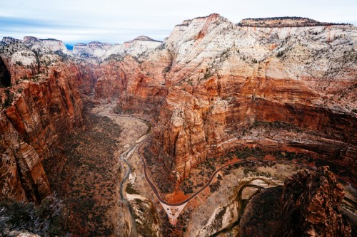 A panoramic view of Zion National Park, showcasing red rock formations and a winding river through a deep canyon.