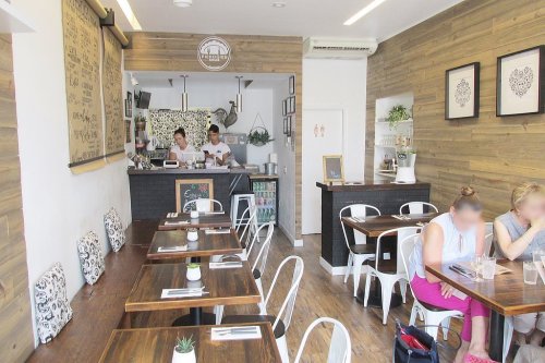 A cozy café interior with wooden walls, tables, and two staff members at the counter. Customers are seated at tables.