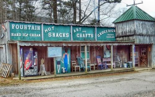 A rustic building with signs for ice cream, crafts, and groceries, featuring rocking chairs on the porch.